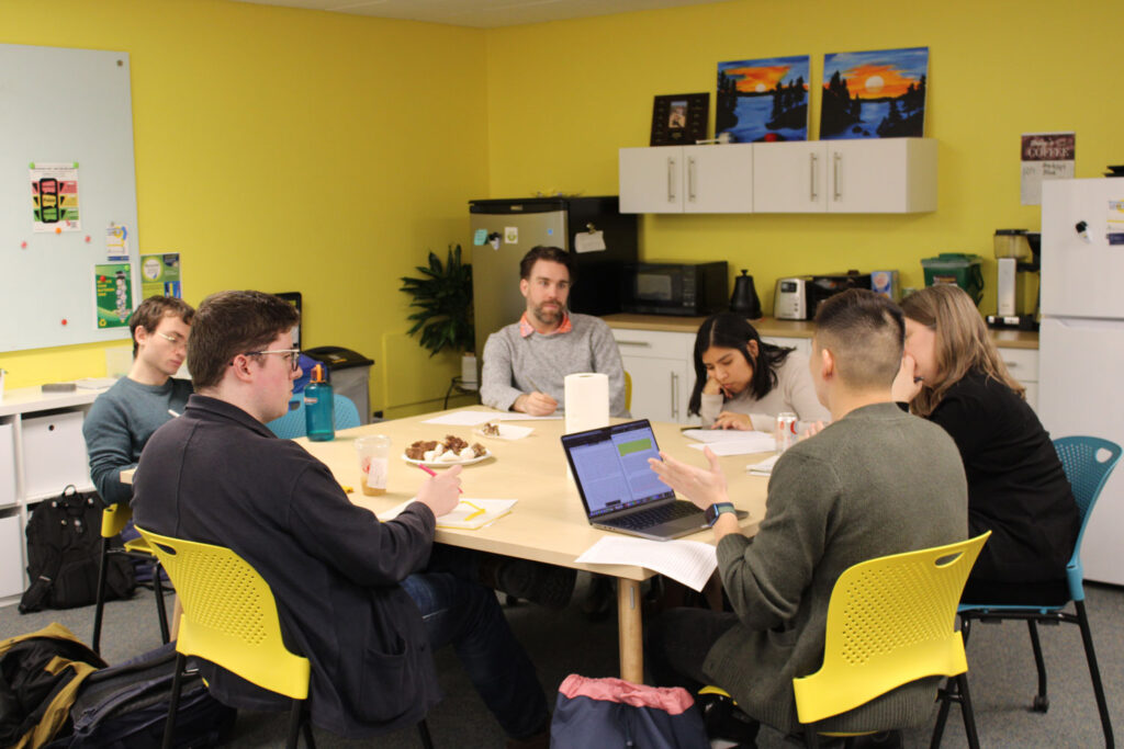 An image of a small working group of students discussing a paper with CID Director Sasha Killewald. They sit at the kitchen table in the center's space. 