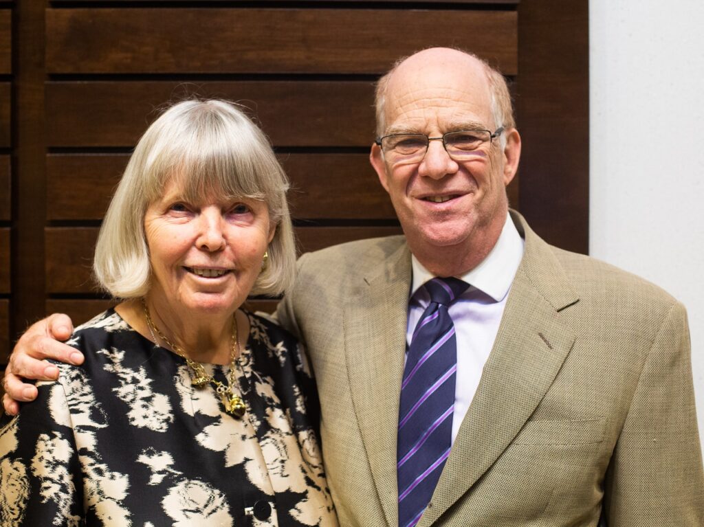 James and Cathleen Stone stand together against a wooden wall.
