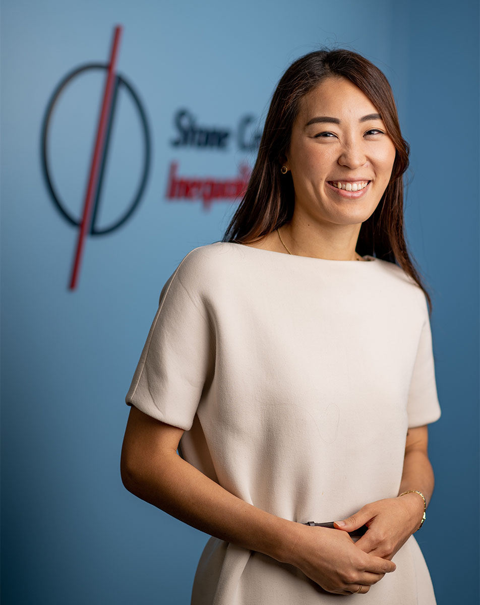 A headshot of Research Assistant Professor Sun Kyoung Lee. She stands in the center with the Stone Center logo behind her in red and blue.