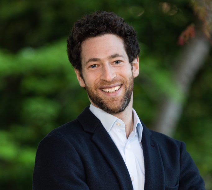 Doron Shiffer-Sebba stands outside, arms crossed, as he faces the camera smiling.